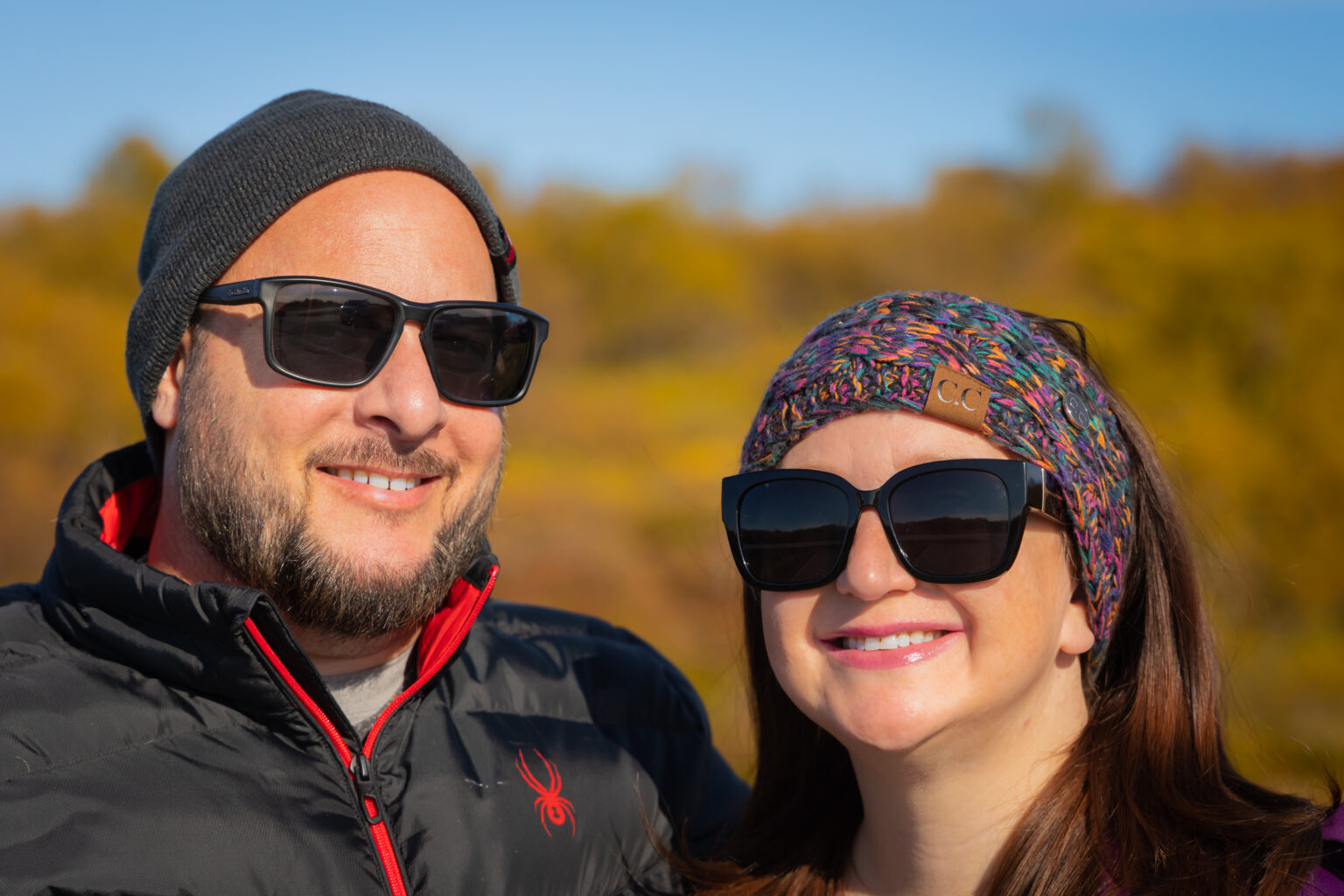 Matt and Michelle smiling outdoors in sunglasses and winter hats.
