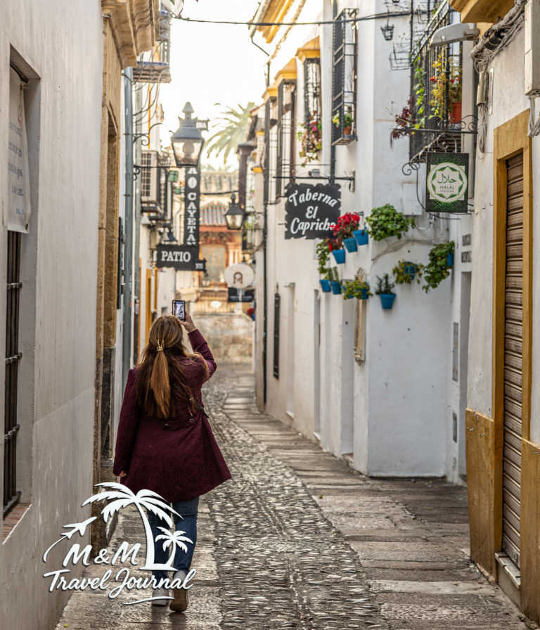 Michelle photographing a narrow cobbled alley lined with white walls and flower pots in Córdoba.